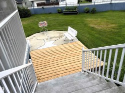 Wood-finish deck with white railings and concrete steps leading to a grass lawn - 
