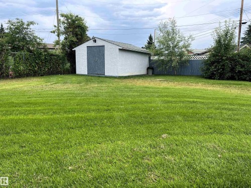 Spacious green lawn with a white storage shed featuring a gray door, mature trees, and perimeter fencing - 4914 51 Ave, Entwistle, AB 