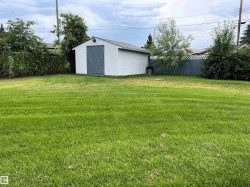 Spacious green lawn with a white storage shed featuring a gray door, mature trees, and perimeter fencing - 
