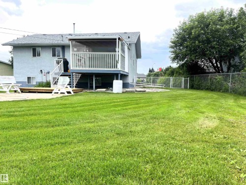 Spacious backyard featuring a manicured lawn, screened-in elevated deck, and lower wood deck - 4914 51 Ave, Entwistle, AB 