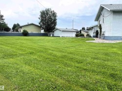 Expansive green lawn with a stucco exterior home featuring a rock-lined foundation bed, a detached garage, and mature trees along the property line - 