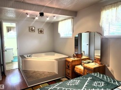 Built-in corner soaking tub with surround, track lighting fixture, two windows with blinds, and wood-finish flooring - 