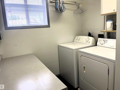 Laundry area featuring a window with blinds, a built-in countertop, and an overhead clothes hanging rod - 4914 51 Ave, Entwistle, AB 