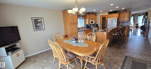 Dining area featuring tile flooring, a multi-light chandelier, and access to a kitchen with wood cabinetry, white appliances, and a breakfast bar - 4221 46 Street, Vegreville, AB 