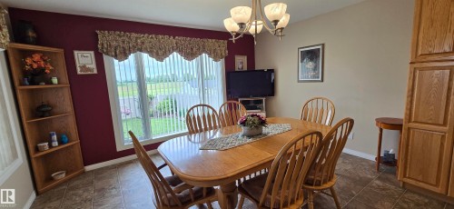 Dining area featuring a large window, tiled flooring, wood-finish cabinetry, and a multi-light chandelier - 4221 46 Street, Vegreville, AB 