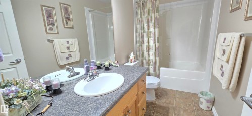 Bathroom featuring a double vanity with built-in sinks, a combined shower and bathtub, tile flooring, and a full-width mirror - 4221 46 Street, Vegreville, AB 