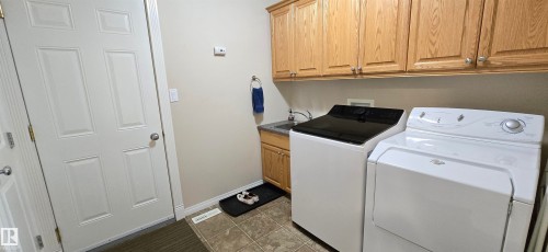 Dedicated laundry area featuring a utility sink with a laminate countertop, wood cabinetry, and tiled flooring - 4221 46 Street, Vegreville, AB 