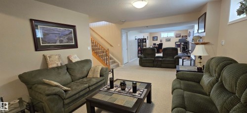 Spacious lower level featuring light-toned carpeting, neutral wall finishes, a wood-finish staircase with white risers, and a built-in wall shelf - 4221 46 Street, Vegreville, AB 