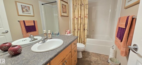 Bathroom featuring a vanity with a laminate countertop and undermount sink, wood-finish cabinetry, a full-width mirror, a toilet, and a combination shower and bathtub - 4221 46 Street, Vegreville, AB 