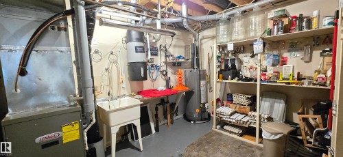 Utility area featuring a Lennox furnace, water heater, utility sink, central vacuum system, and extensive built-in shelving - 4221 46 Street, Vegreville, AB 