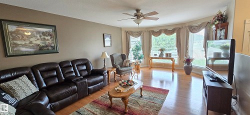 Spacious living area featuring wood-finish flooring, a ceiling fan with integrated lighting, and a bay window with decorative valances - 4221 46 Street, Vegreville, AB 