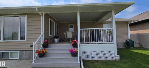 Rear covered patio with white railings, lattice skirting, and concrete steps - 4221 46 Street, Vegreville, AB 