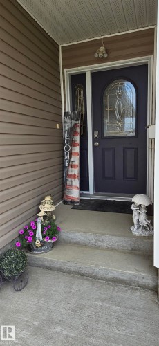 Entryway featuring a dark paneled door with an arched glass insert, sidelight, and textured vinyl siding - 4221 46 Street, Vegreville, AB 