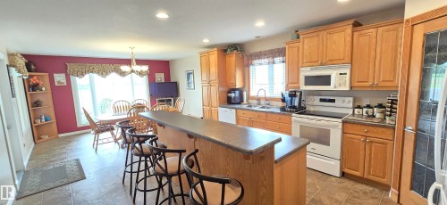 Spacious kitchen featuring wood cabinetry, white appliances, and a central island with bar seating - 4221 46 Street, Vegreville, AB 