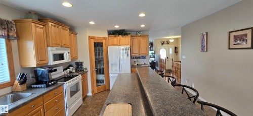 Kitchen featuring light wood cabinetry, white appliances, recessed lighting, and a multi-level breakfast bar with seating - 4221 46 Street, Vegreville, AB 