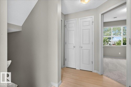 Hallway featuring wood-finish flooring, a flush-mount ceiling light, and two white paneled closet doors - 20 4821 Terwillegar Common, Edmonton, AB 