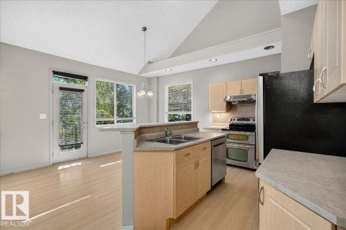Open-concept kitchen and living area featuring wood-finish flooring, vaulted ceilings, and recessed lighting - 20 4821 Terwillegar Common, Edmonton, AB 