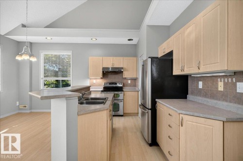 Kitchen featuring light wood-finish cabinetry, stainless steel appliances, a double basin sink, and a breakfast bar - 20 4821 Terwillegar Common, Edmonton, AB 