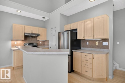 Kitchen featuring light wood cabinetry, a breakfast bar, recessed lighting, tile backsplash, and stainless steel appliances - 20 4821 Terwillegar Common, Edmonton, AB 