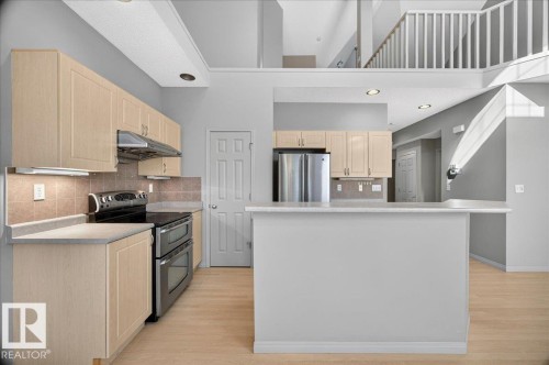 Kitchen featuring light wood-finish cabinetry, a dual-oven range, a stainless steel refrigerator, and a breakfast bar - 20 4821 Terwillegar Common, Edmonton, AB 
