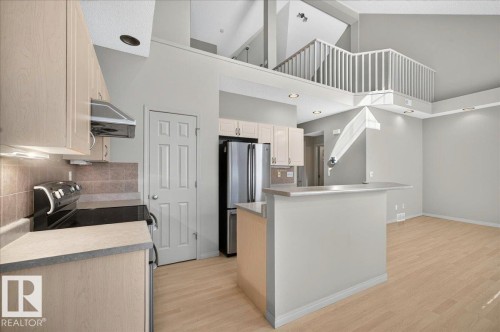 Open-concept kitchen and living area featuring a breakfast bar, light wood-finish flooring, recessed lighting, and a second-story interior balcony with white railings - 20 4821 Terwillegar Common, Edmonton, AB 