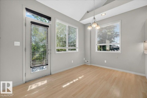 Bright dining area featuring wood-finish flooring, multiple windows with blinds, a glass-paned exterior door, and a multi-bulb chandelier - 20 4821 Terwillegar Common, Edmonton, AB 
