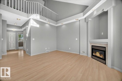 Spacious interior featuring wood-finish flooring, a contemporary fireplace with a stone surround, and an integrated media niche - 20 4821 Terwillegar Common, Edmonton, AB 