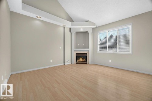 Spacious room featuring wood-finish flooring, a built-in corner fireplace, a large window with horizontal blinds, and ceiling-mounted recessed lighting - 20 4821 Terwillegar Common, Edmonton, AB 