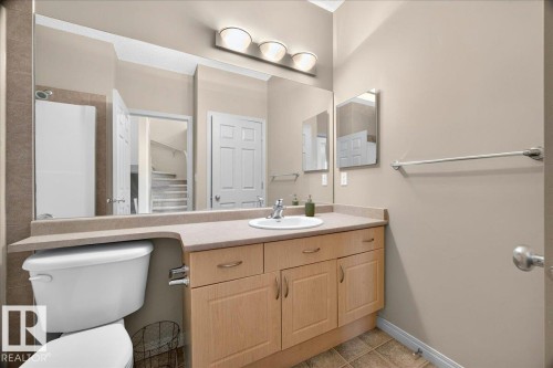 Bathroom featuring a vanity with a light-toned countertop and integrated sink, wood-finish cabinetry, and a large wall-mounted mirror - 20 4821 Terwillegar Common, Edmonton, AB 