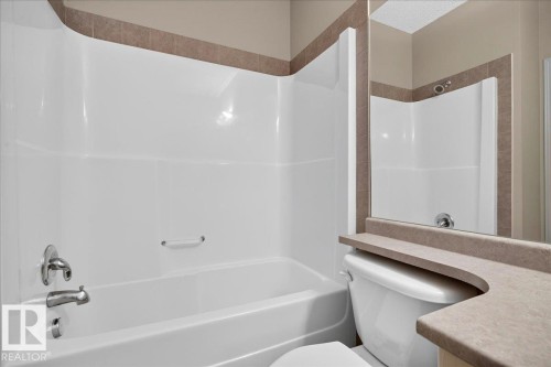 Bathroom featuring a white tub/shower combination with chrome fixtures, a toilet, and a countertop with an integrated backsplash - 20 4821 Terwillegar Common, Edmonton, AB 