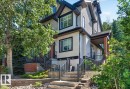 Multi-story residence featuring light-colored siding, black trim windows, a covered front porch with brick columns, and a terraced front yard with stone steps and retaining walls - 20 4821 Terwillegar Common, Edmonton, AB 