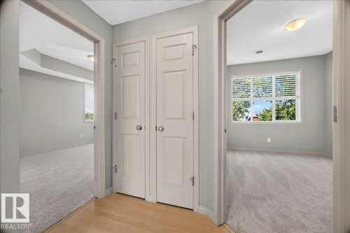 Central hallway with light wood-finish flooring, two panel doors, and two rooms featuring light gray walls, light gray carpeting, and window blinds - 20 4821 Terwillegar Common, Edmonton, AB 