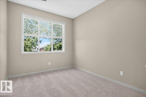 Neutral-toned room featuring a large window with white blinds, light beige carpeting, and painted walls - 20 4821 Terwillegar Common, Edmonton, AB 