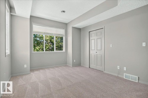 Spacious room featuring neutral carpeting, light gray wall finishes, and a large multi-pane window with horizontal blinds - 20 4821 Terwillegar Common, Edmonton, AB 