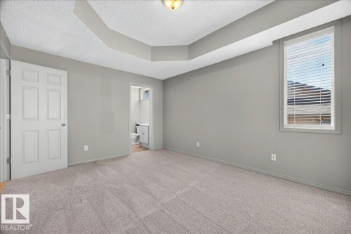 Spacious room featuring tray ceilings, neutral carpeting, and a window with horizontal blinds - 20 4821 Terwillegar Common, Edmonton, AB 