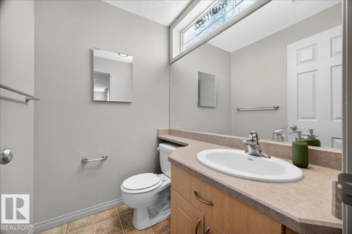 Bathroom featuring an integrated vanity sink with a laminate countertop, light wood-finish cabinetry, and a full-width wall mirror - 20 4821 Terwillegar Common, Edmonton, AB 