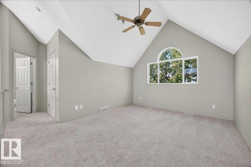 Carpeted room featuring a vaulted ceiling with a ceiling fan, a large arch-top window, a white paneled door, and neutral-toned walls - 20 4821 Terwillegar Common, Edmonton, AB 