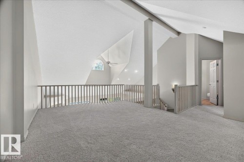 Spacious loft area featuring light gray carpeting, a vaulted ceiling with exposed beams, and a decorative arched window - 20 4821 Terwillegar Common, Edmonton, AB 