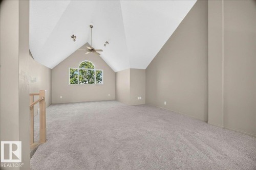 Open loft space featuring vaulted ceilings, a prominent arched window, and neutral wall-to-wall carpeting - 20 4821 Terwillegar Common, Edmonton, AB 