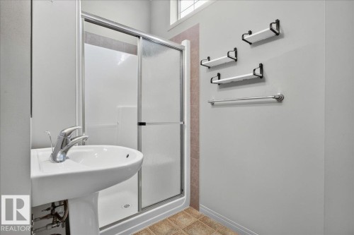 Pedestal sink with chrome faucet, enclosed shower with sliding glass doors, three wall-mounted shelves, and a towel bar - 20 4821 Terwillegar Common, Edmonton, AB 