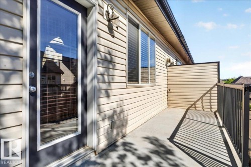 Balcony featuring light-colored siding, a full-lite exterior door with a dark frame, two windows with horizontal blinds, and a durable metal railing - 20 4821 Terwillegar Common, Edmonton, AB 
