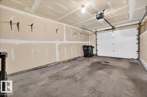 Interior garage space featuring a concrete floor, an overhead garage door, and a ceiling-mounted garage door opener - 20 4821 Terwillegar Common, Edmonton, AB 