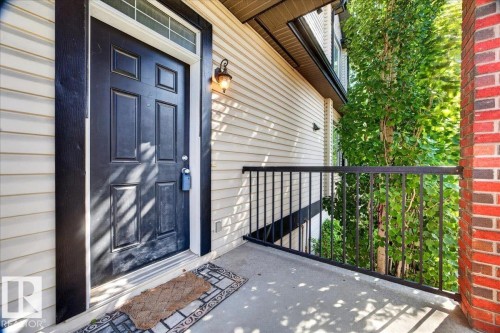 Panel-style entry door with transom window, complemented by an exterior wall sconce - 20 4821 Terwillegar Common, Edmonton, AB 