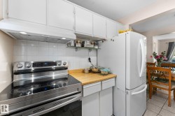 Kitchen featuring white cabinetry, a stainless steel range with a flat cooktop, white tile backsplash, wood-finish countertops, and a white refrigerator - 
