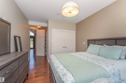 Spacious bedroom featuring wood-finish flooring, a contemporary ceiling light fixture, and a built-in closet with double panel doors - 