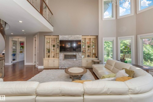 Two-story living room featuring expansive windows, wood-finish flooring, a contemporary fireplace with stone surround, and built-in shelving - 3503 Watson Point(E), Edmonton, AB 