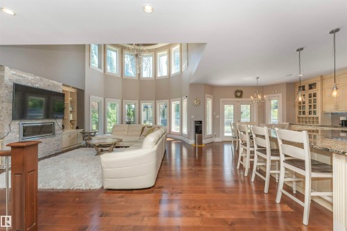 Hardwood flooring throughout the open-concept living space, featuring a stone-clad fireplace, integrated cabinetry, and a curved wall of windows - 3503 Watson Point(E), Edmonton, AB 