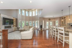 Hardwood flooring throughout the open-concept living space, featuring a stone-clad fireplace, integrated cabinetry, and a curved wall of windows - 
