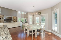 Open-concept living space featuring wood-finish flooring, a stone-accented fireplace surround, built-in shelving, a chandelier, and double patio doors - 
