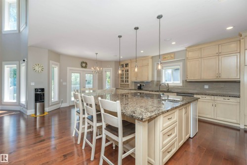 Expansive kitchen featuring a large island with an undermount sink and three pendant lights, ample cabinetry, a tiled backsplash, and wood-finish flooring - 3503 Watson Point(E), Edmonton, AB 
